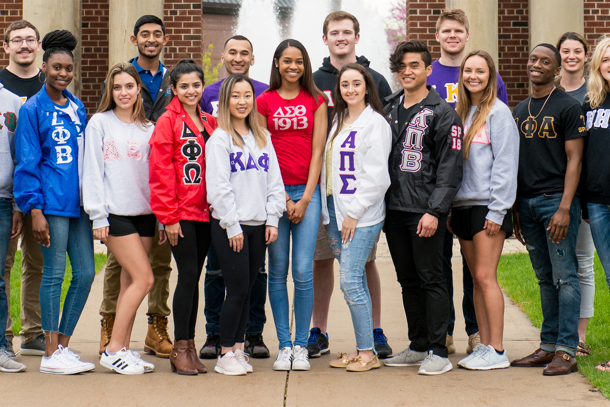 Group of Greek students wearing their chapter apparel posing in front of Hallene Gateway.
