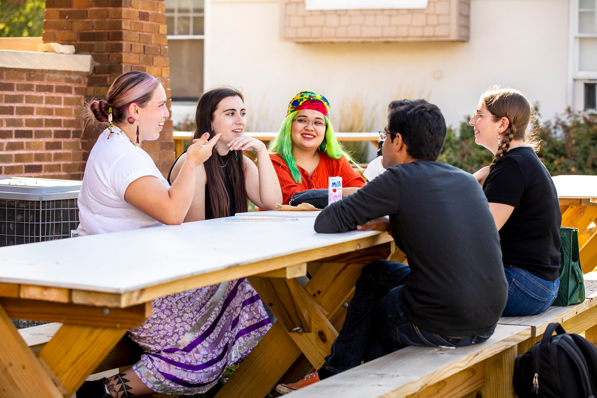 Group of students sitting and talking at table outside of the Native American House