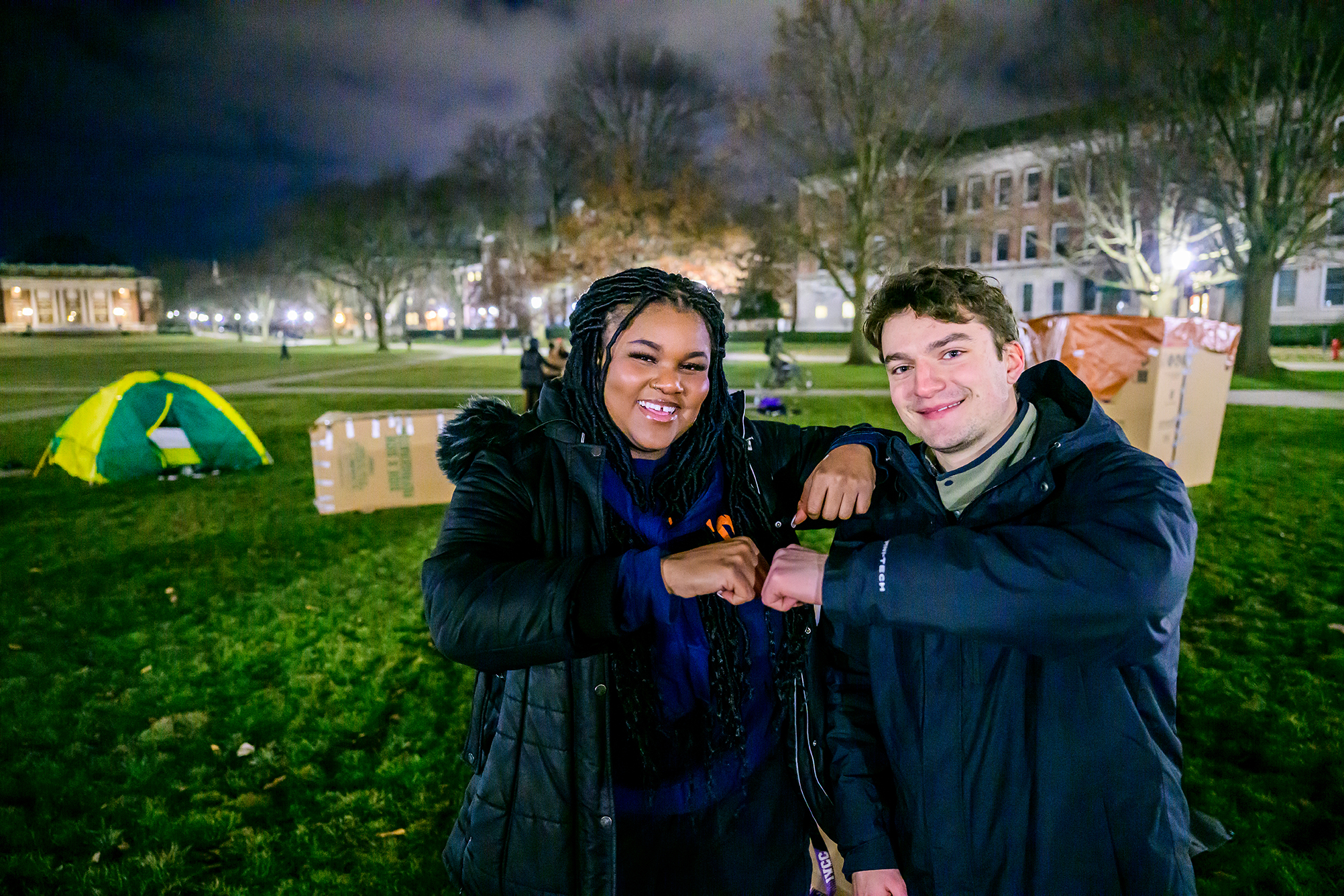 Two students fist bump during One Winter Night event with Main Quad in background