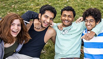 Four diverse students smiling with arms around each other
